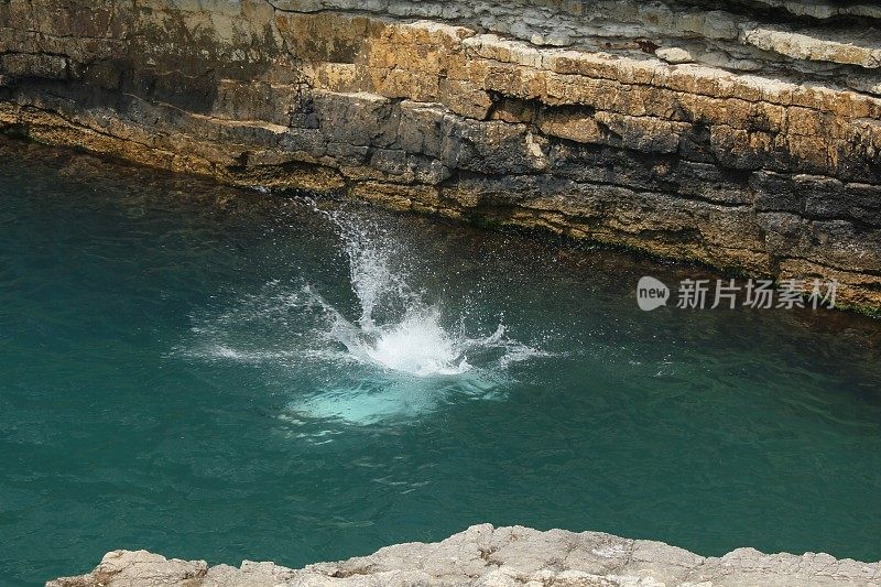 在Kerpe Kartal Kayaları，有人从岩石跳进海里，溅起的水花和泡沫